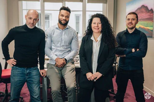Quatre personnes posent ensemble dans un bureau.