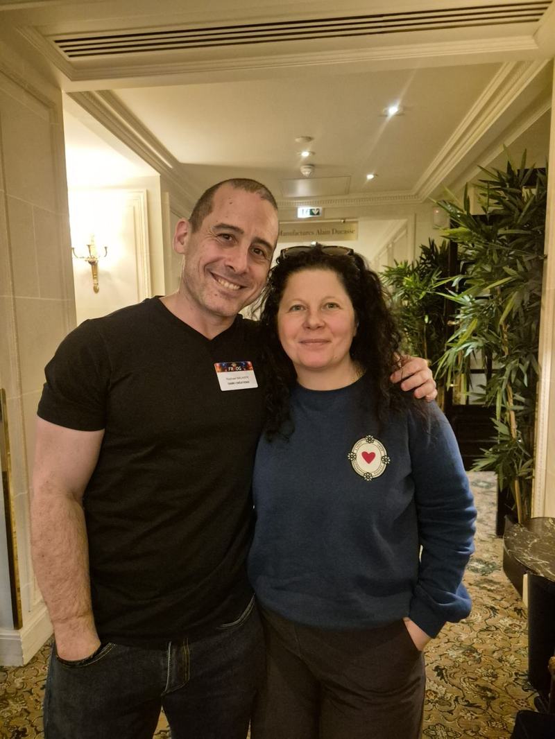 Photo d’un homme et d’une femme qui posent côte à côte, souriants, dans un couloir ; l’homme porte un badge FRnOG au nom de Raphael Maunier.