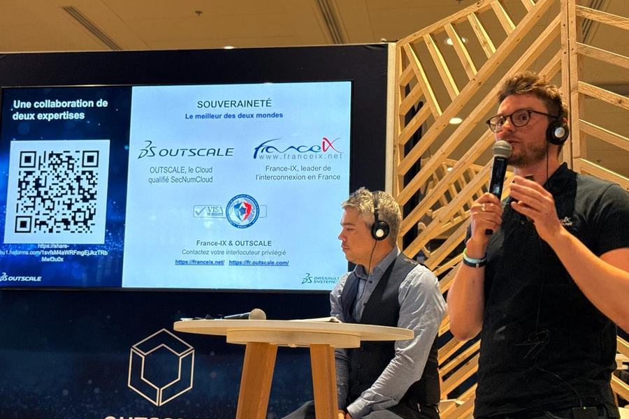 Sur une scène marquée « OUTSCALE », un homme parle au micro à côté d’un homme assis, devant un écran qui affiche « Une collaboration de deux expertises », « Souveraineté, le meilleur des deux mondes » et les logos d’OUTSCALE et de France-IX.