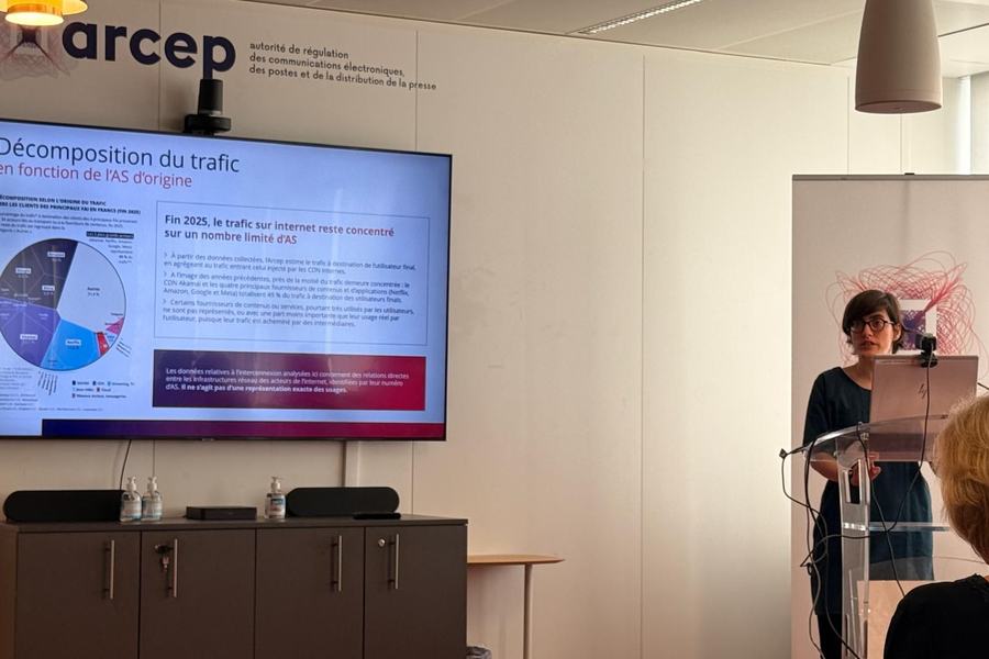 Conférence de l’Arcep : une intervenante au pupitre, à côté d’un écran affichant « Décomposition du trafic en fonction de l’AS d’origine ».