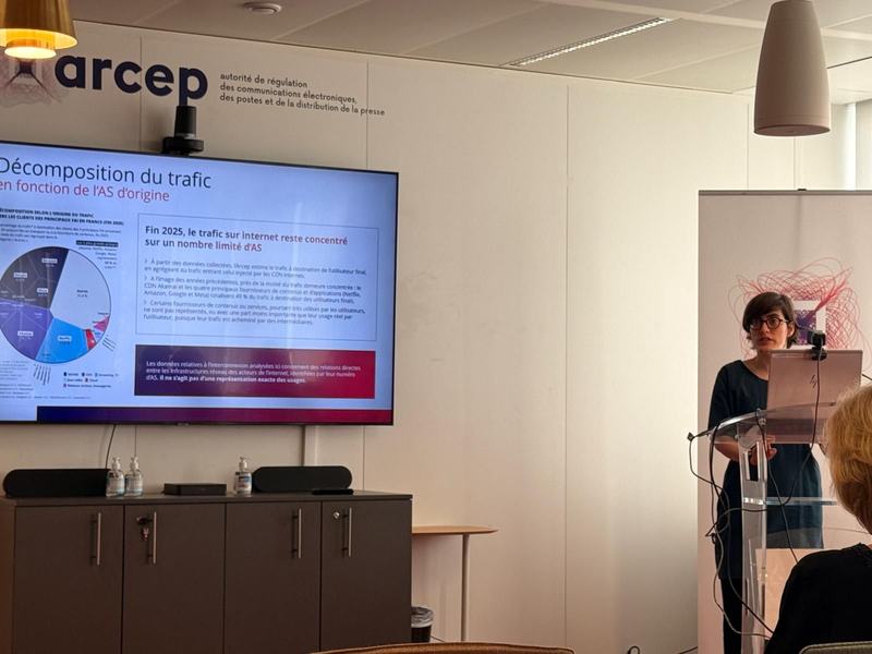 Conférence de l’Arcep : une intervenante au pupitre, à côté d’un écran affichant « Décomposition du trafic en fonction de l’AS d’origine ».
