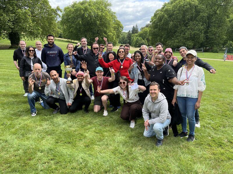 Photo de groupe sur une pelouse, devant de grands arbres : les participants, médailles au cou, posent avec une coupe.