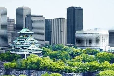 Un château japonais entouré d’arbres, devant des tours de bureaux.