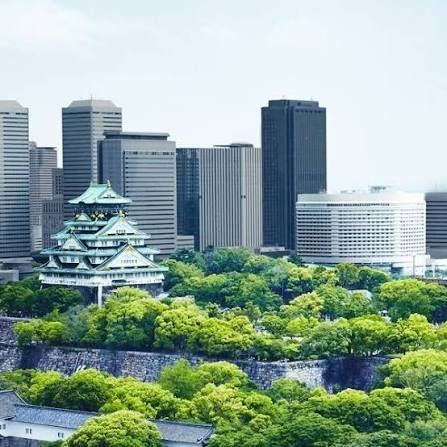 Un château japonais entouré d’arbres, devant des tours de bureaux.